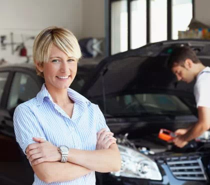 uśmiechnięta kobieta przed naprawianym samochodem w warsztacie